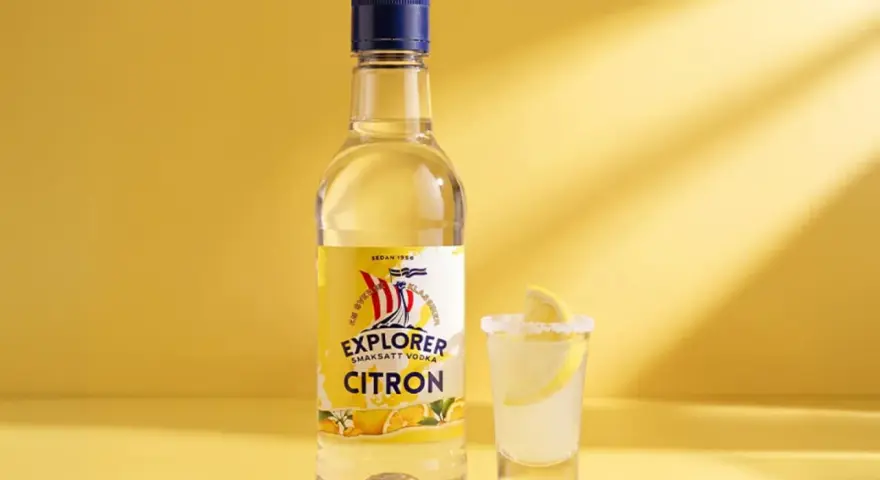 En flaska Explorer Citron vodka bredvid ett glas med en lemon drops shot, garnerad med citronskiva och saltkant.