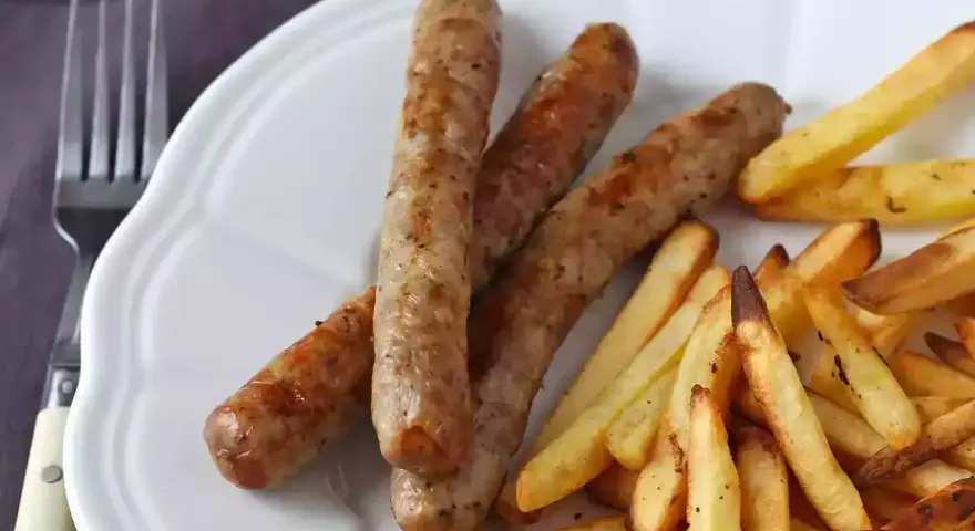 Saftig korv i airfryer med krispiga pommes frites på en vit tallrik. Enkel och god middag.