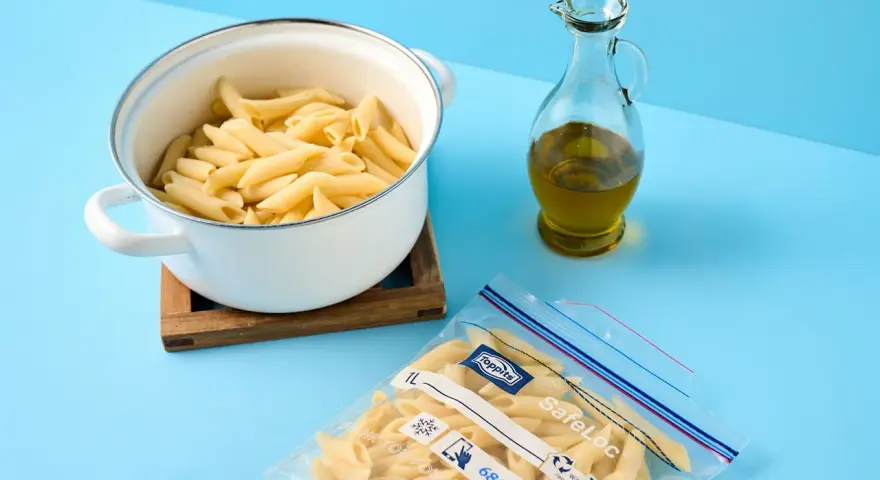 Koka pasta och förbered för att frysa in den. En kastrull med penne, en flaska olivolja och en fryspåse syns.