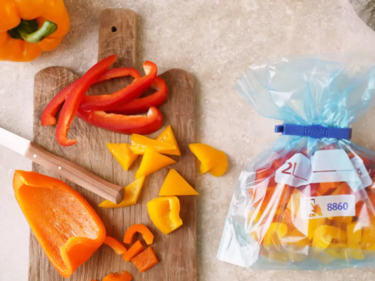 F&ouml;rbereder f&ouml;r att frysa paprika. Skurna bitar av r&ouml;d, gul och orange paprika ligger p&aring; en sk&auml;rbr&auml;da bredvid en frys-p&aring;se fylld med paprika.