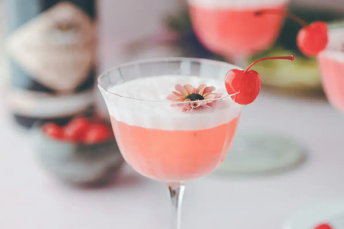 En rosa drink, en Pink Lady, med skum och en k&ouml;rsb&auml;rsdekoration.