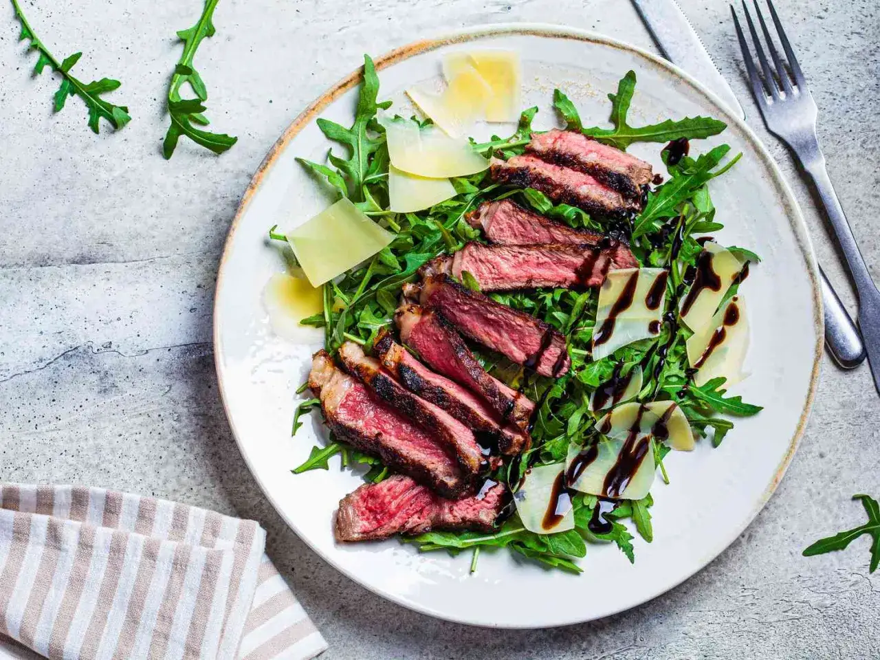 En tallrik med saftig biff tagliata, rucola, parmesan och balsamvin&auml;gerdressing.