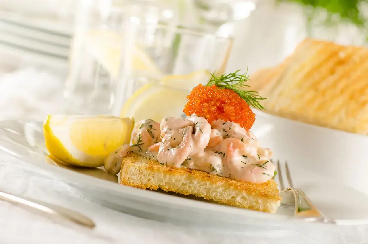 En kr&auml;mig skagen toast med r&auml;kor, dill och rom, garnerad med dillkvist och citronklyfta.