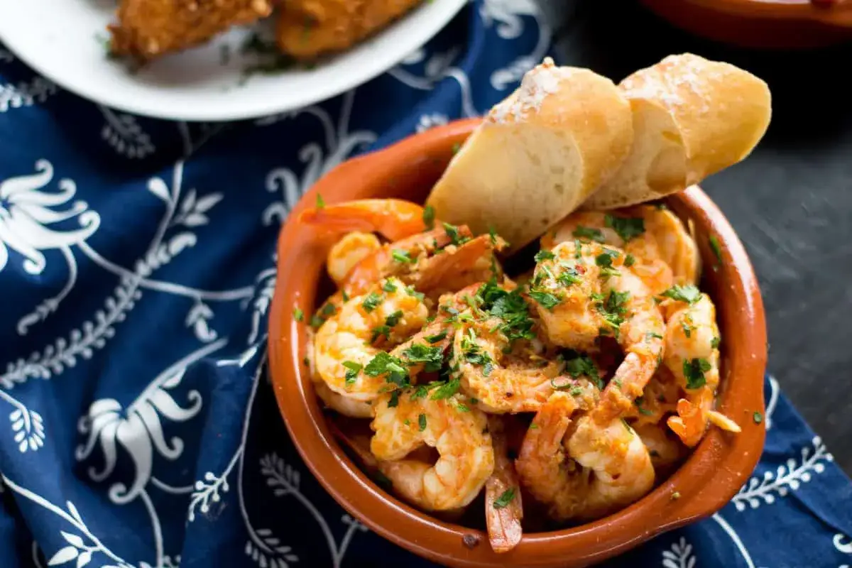 En skål med saftiga gambas, perfekt för ett snabbt gambas recept. Serveras med krispigt bröd och en blå blommig duk.