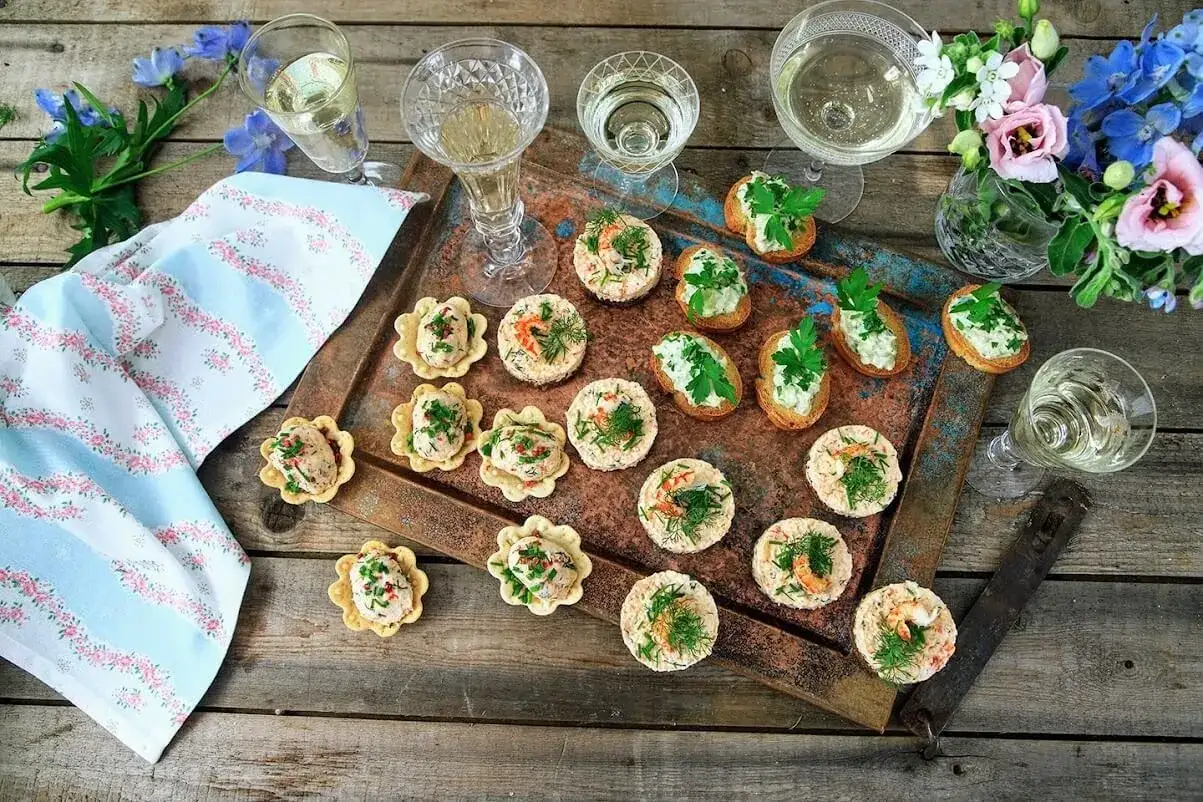 Små, läckra snacks till bubbel, serverade på ett fat med blommor och glas. Perfekt för festen!