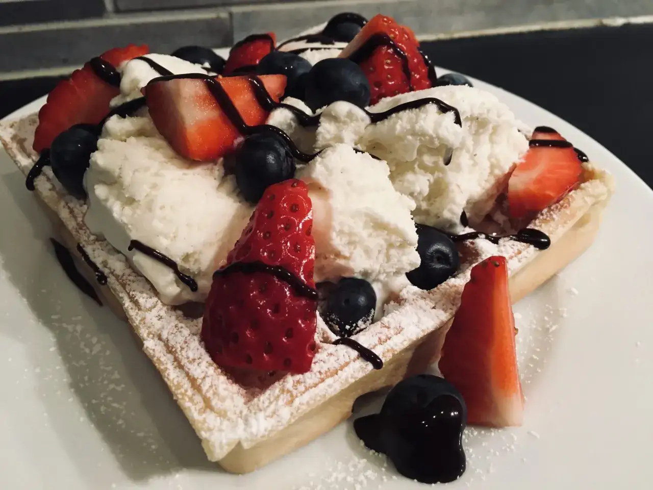 En belgisk våffla toppad med glass, jordgubbar, blåbär och chokladsås. Ett perfekt recept för en lyxig frukost eller dessert.