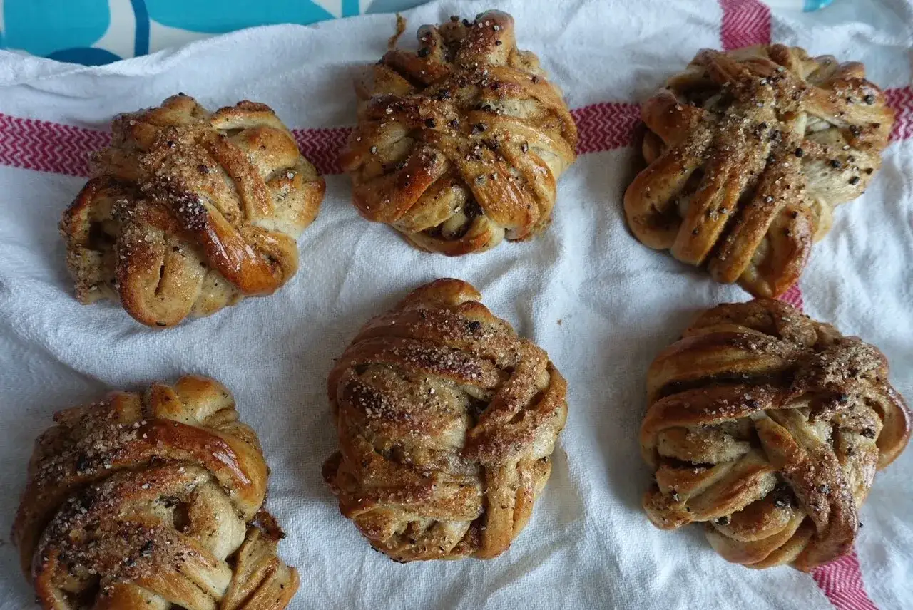 Sex vackert fl&auml;tade bullar med mandelmassa, str&ouml;sslade med socker och kanel, ligger p&aring; en vit handduk med r&ouml;da r&auml;nder.