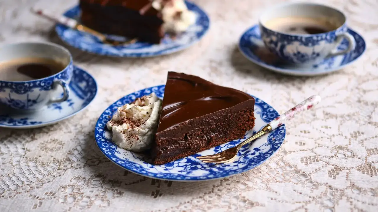 En bit kladdig kladdkaka med vispgr&auml;dde p&aring; en bl&aring;vit tallrik, bredvid en kopp kaffe.
