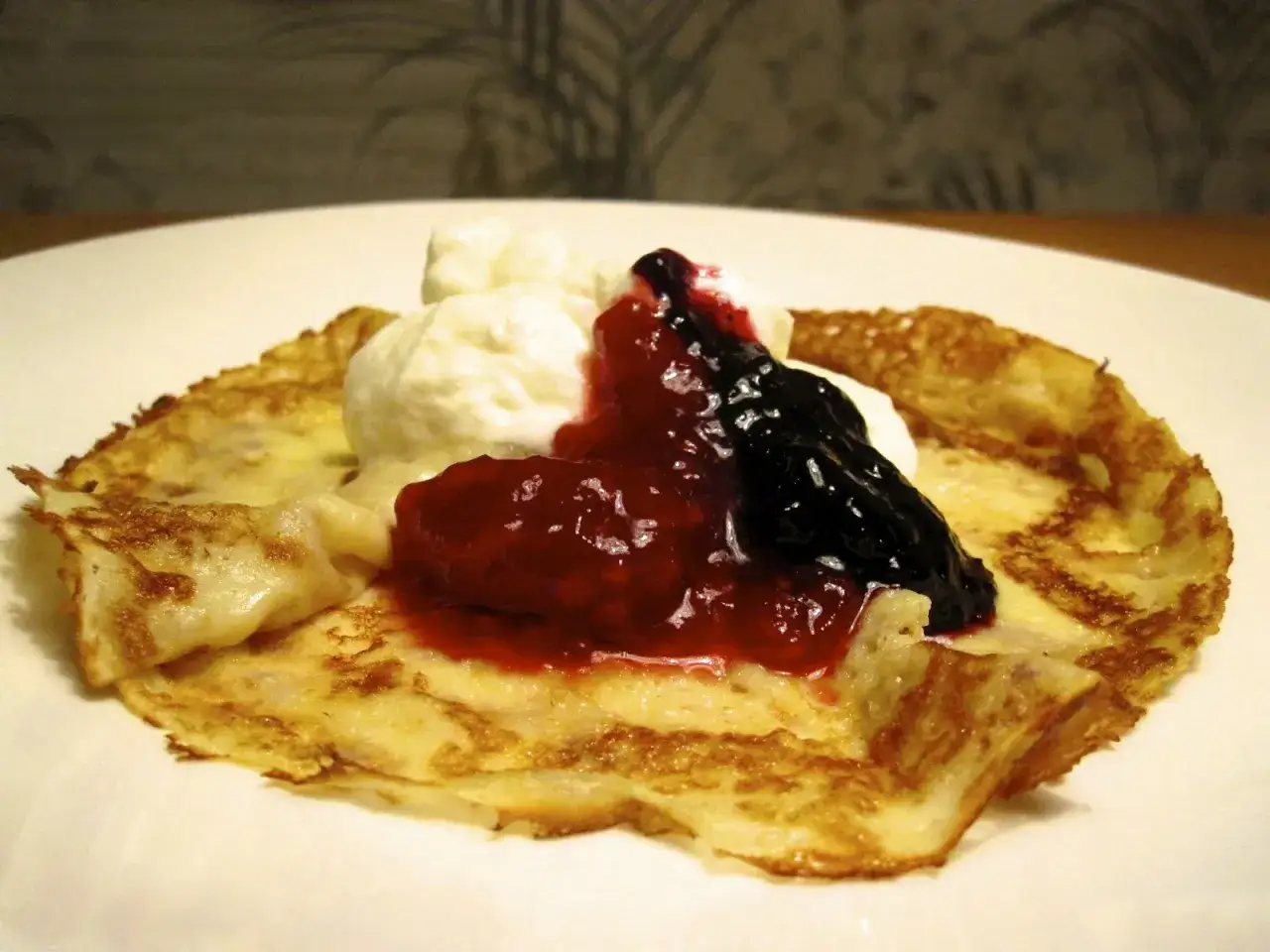 En gyllene pannkaka toppad med vispad gr&auml;dde, hallonsylt och bl&aring;b&auml;rssylt. Ett perfekt pannkakor recept f&ouml;r en fika.
