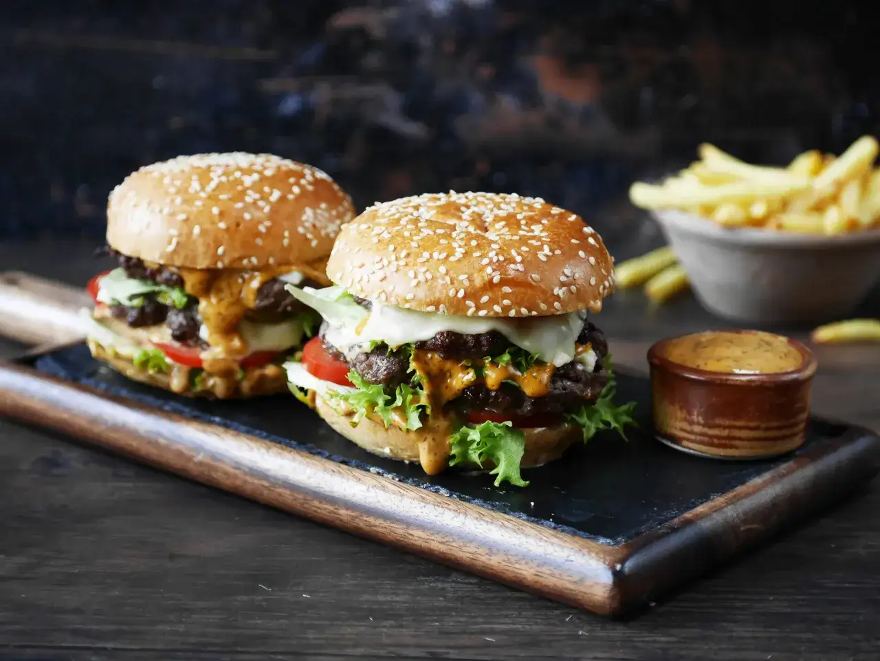 Två saftiga hamburgare med sesamfrön, ost, sallad och tomat, serverade med pommes frites och dippsås. Perfekt hamburgare i airfryer!