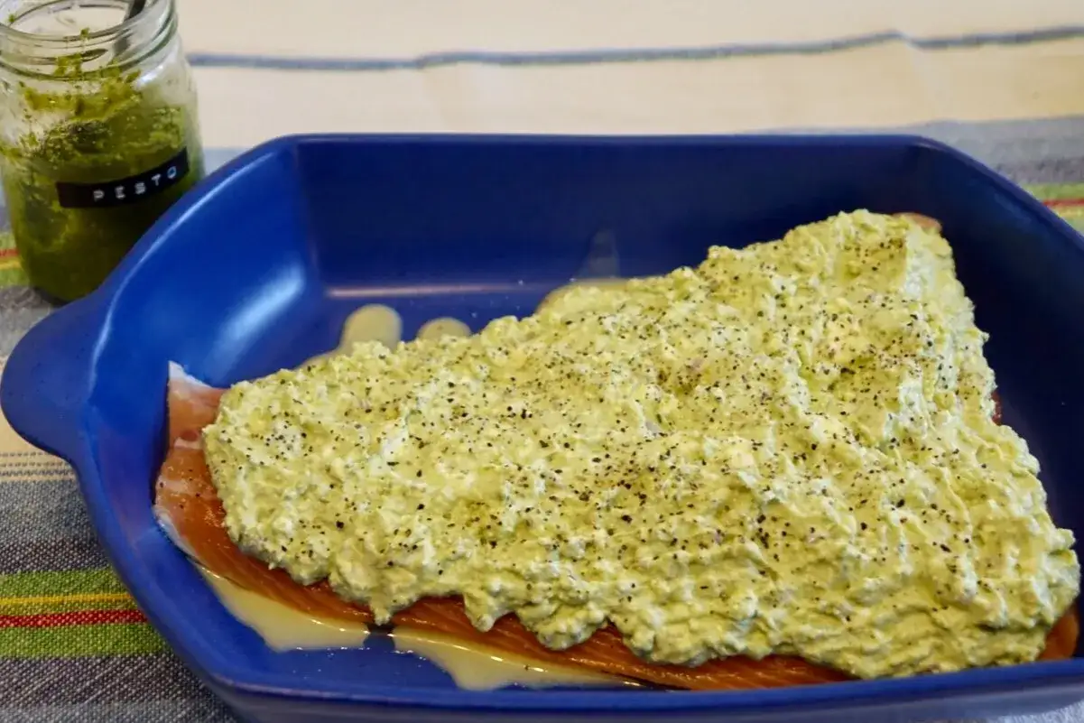 Lax med pesto och fetaost i bl&aring; form, redo f&ouml;r ugnen. En burk med pesto syns i bakgrunden.