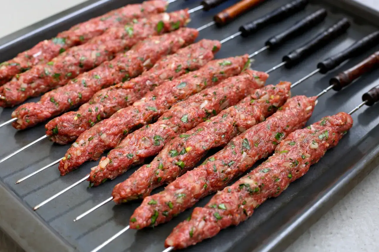 Råa adana kebab-spett med lök och persilja, redo för grillen.