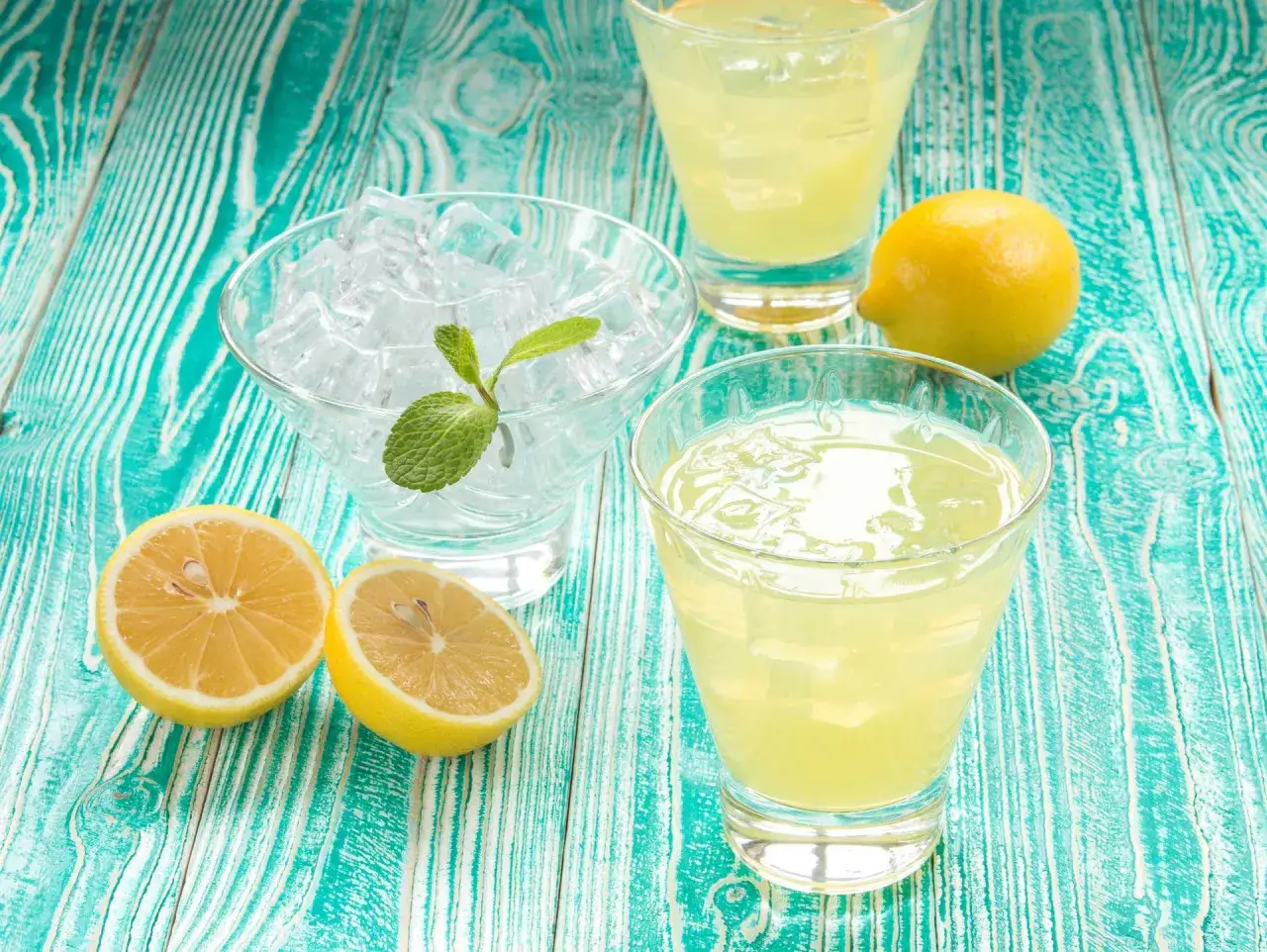 Färska citroner, is och mynta för ett perfekt limoncello recept. Två glas med den gyllene drycken står redo.