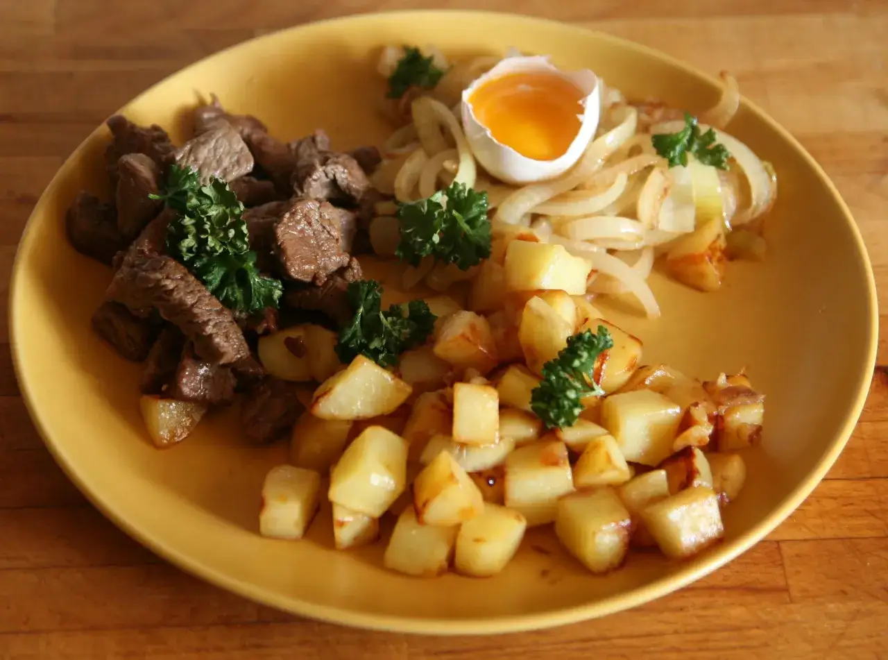 En tallrik med stekt k&ouml;tt, stekt potatis, stekt l&ouml;k och ett l&ouml;skokt &auml;gg. Ett klassiskt husmanskost recept som passar perfekt f&ouml;r en vardagsmiddag.