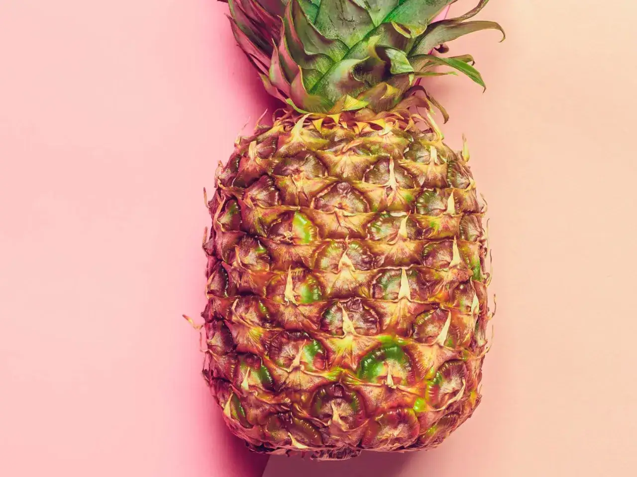 En ananas med taggig yta och gröna blad på en rosa bakgrund. Tänk att dela ananas utan kniv!