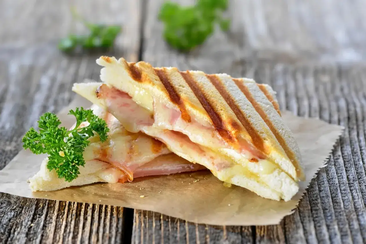 En perfekt grillad croque monsieur med sm&auml;lt ost och skinka, garnerad med persilja, serverad p&aring; brunt papper.