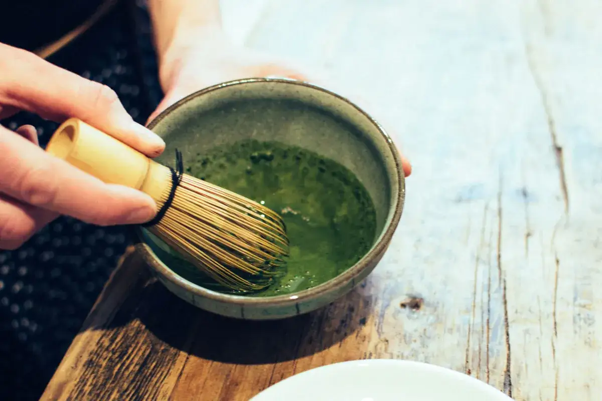 En hand vispar intensivt grönt matcha i en skål, redo att uppleva hur smakar matcha.