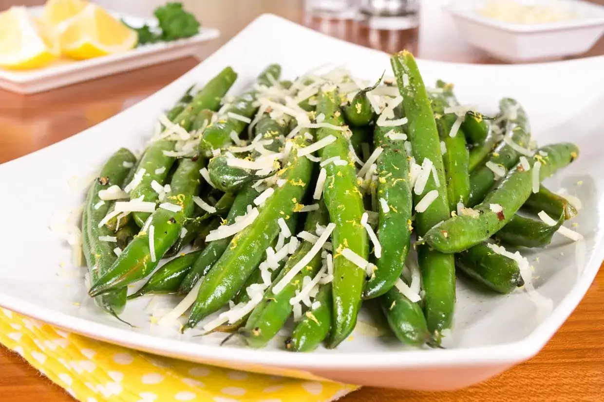 En vit skål med gröna haricots verts, toppade med riven parmesan och citronskal. En läcker sidorätt.