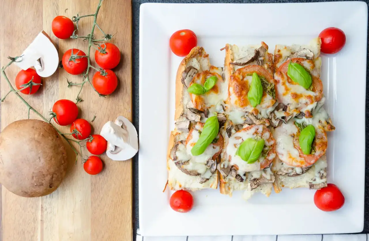 En härlig bruschetta med mozzarella, tomater och svamp, toppad med färsk basilika. Ingredienserna ligger bredvid på en skärbräda.