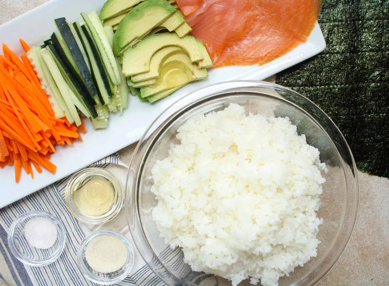 Förberedelser för hemmagjord sushi: ris, lax, avokado, gurka, morot och nori.