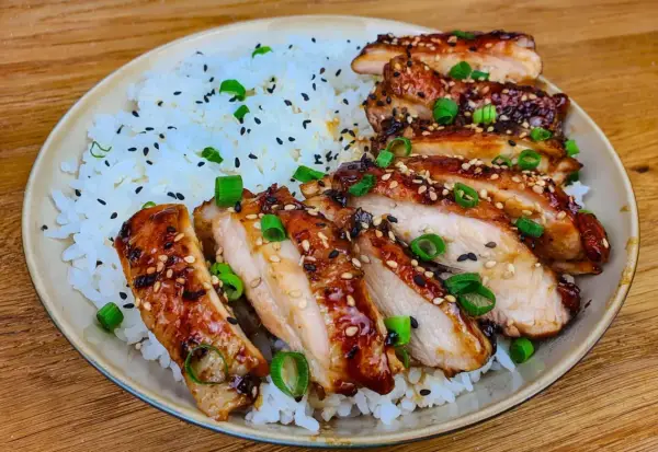 Skivad kyckling i gochujang marinad, serverad med ris och toppad med sesamfrön och salladslök. En härlig rätt som lockar smaklökarna.