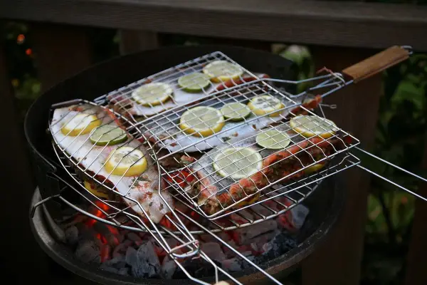 Grillad fisk med citron- och limeskivor på en kolgrill. Doften av sommar och god mat sprider sig.