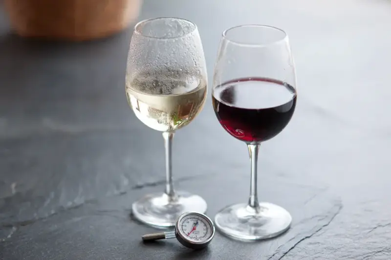 Två glas vin, ett vitt och ett rött, med en termometer bredvid. Perfekt vitt vin temperatur är viktigt för njutning.